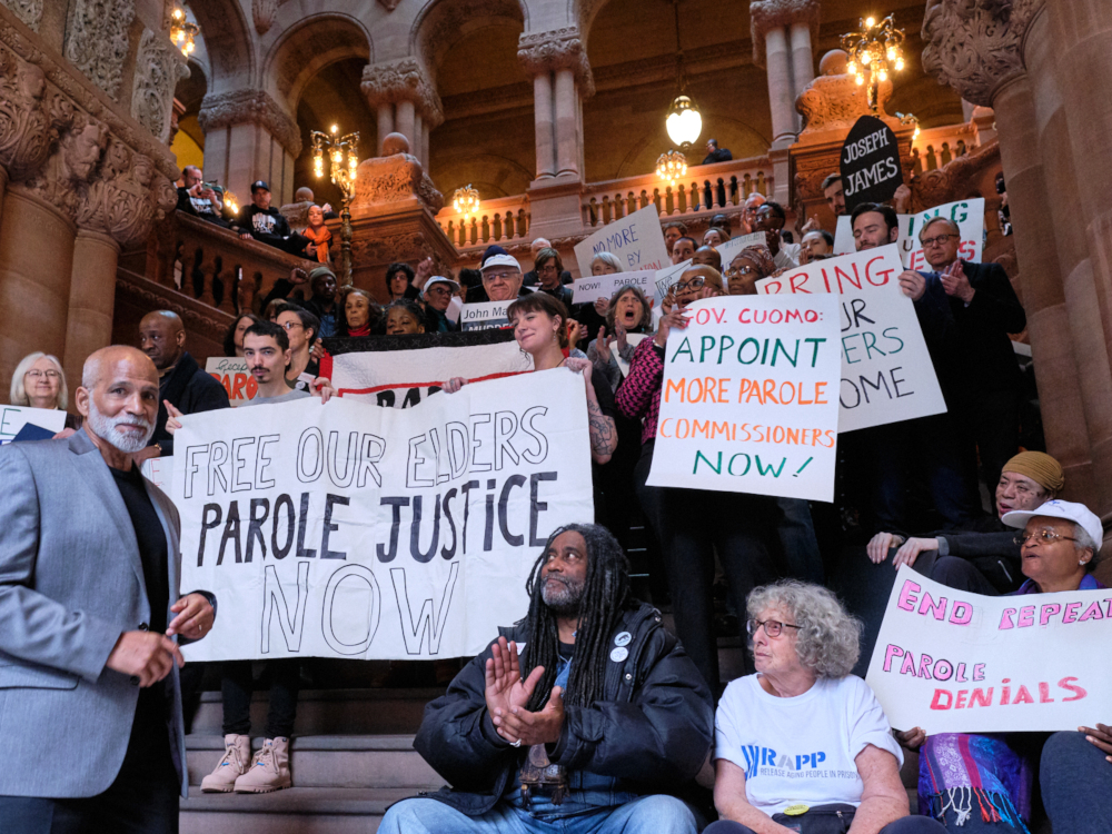 A crowd of people standing on a stairwell in the state Capitol holding signs that say, "Parole Justice."