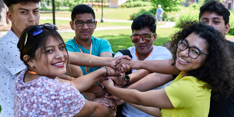 Young people standing in a circle, putting their hands in the middle.