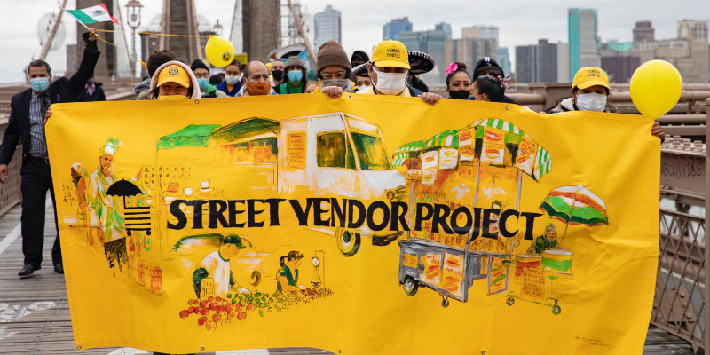 Photo of Street Vendor Project members marching with a large yellow banner with their logo.